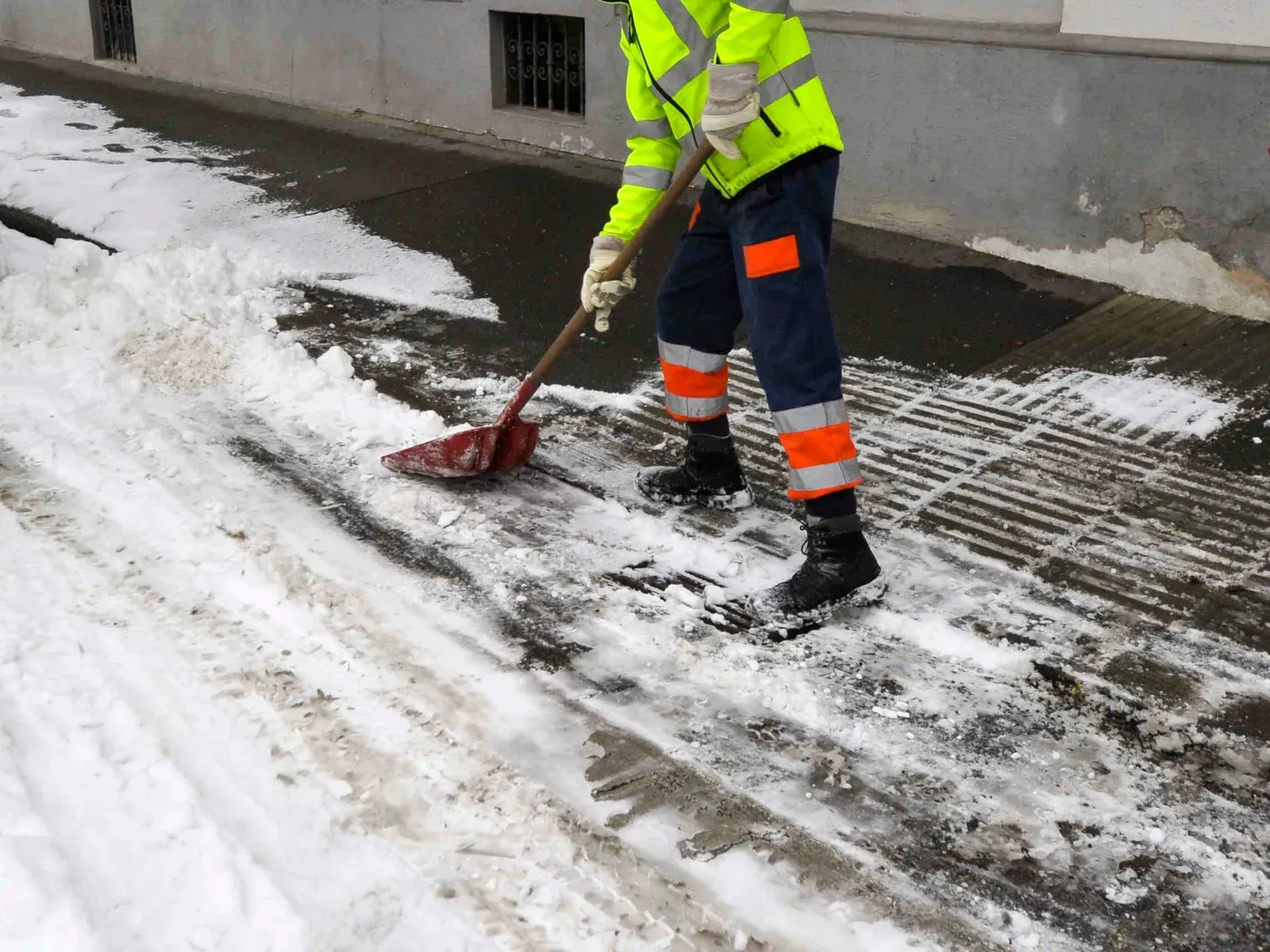 A man is shoveling snow from the sidewalk with a shovel.