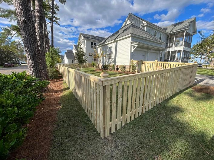 A wooden picket fence is in front of a house.