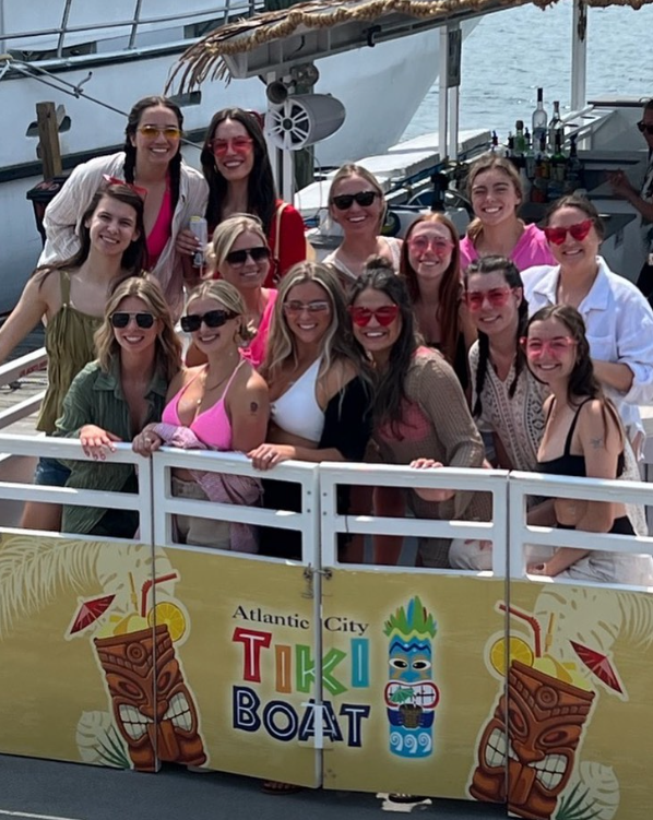 Group of people on an Atlantic City Tiki Boat. Smiling, wearing sunglasses, posing for a photo.