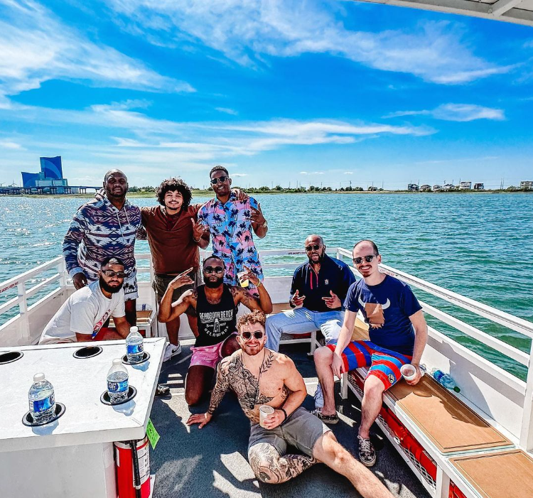 Group of people on a boat, posing for a photo under a blue sky, water in the background.