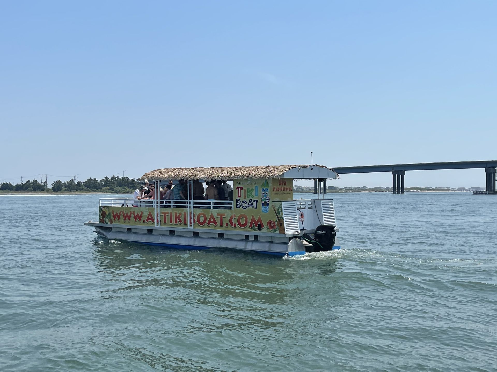 Tiki boat on water with passengers; bridge in background.