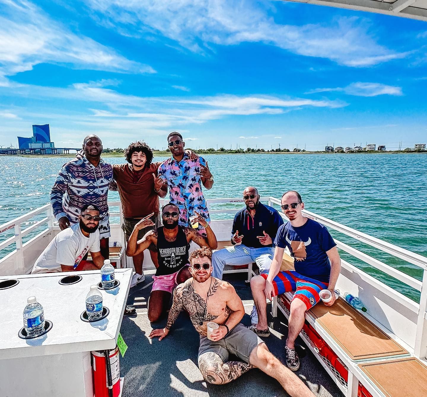 Group of people on a boat, smiling, posing in front of water and blue sky.