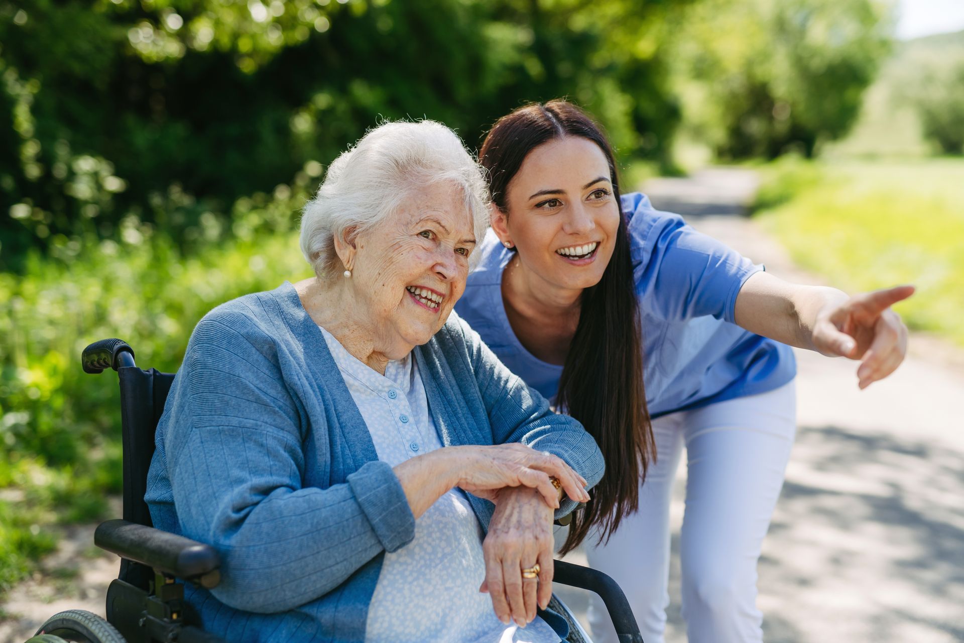 Woman in wheelchair smiles while another woman points ahead on a path