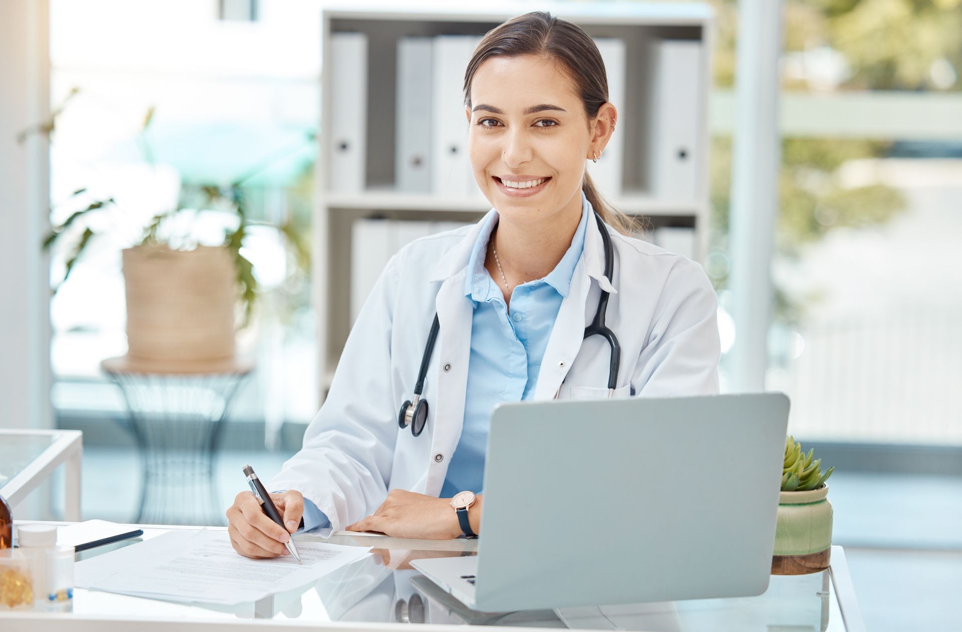 Una médica está sentada en un escritorio frente a una computadora portátil.
