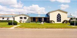 A one-story building with a light-colored exterior, blue metal roof, and a large arched window on the right wing.