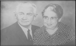 A black and white portrait of a person in a suit and tie standing next to a person wearing a polka-dot collared shirt.