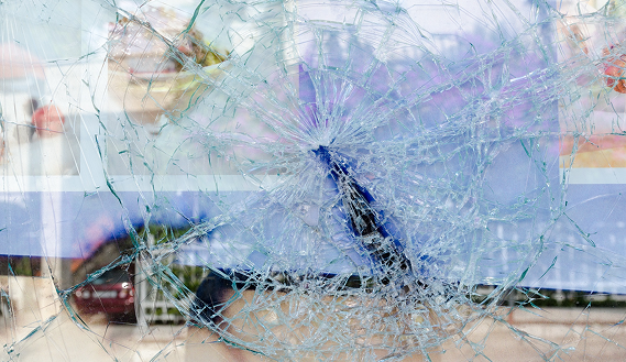 A close-up view of a large, shattered glass panel featuring a dense web of cracks radiating from a central impact point.