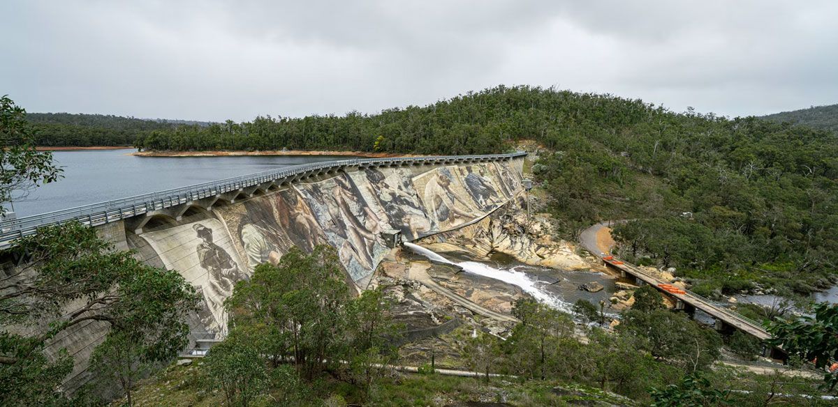 Dam spillway beside a lake, with water and debris in a green hillside landscape