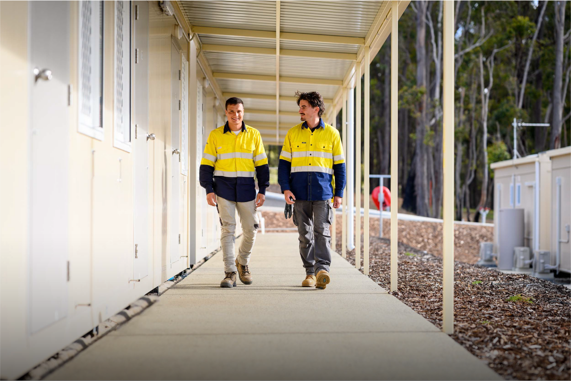 Two people in high-visibility vests walk down a covered walkway in Collie Hills Village.