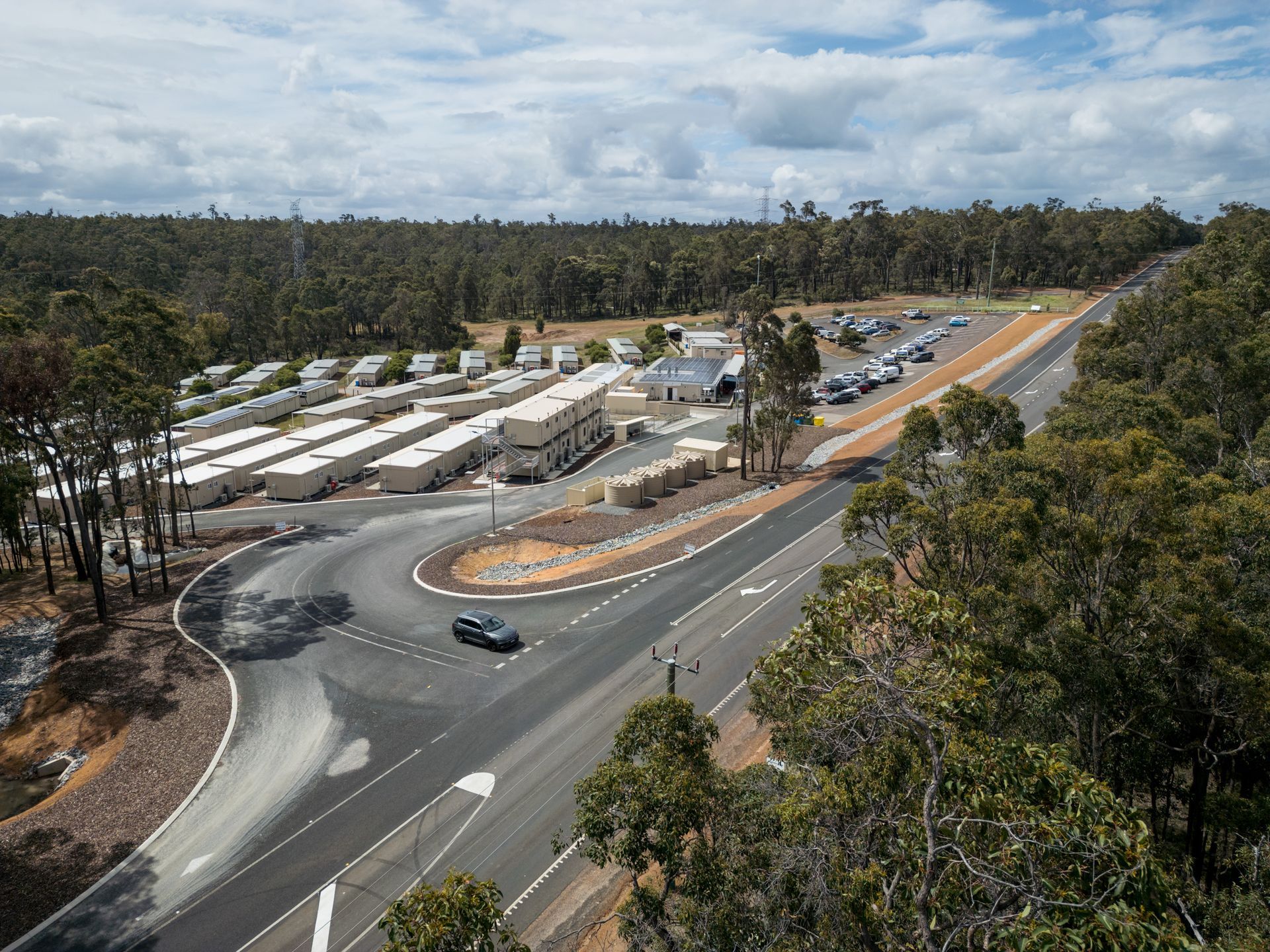 Aerial view of Collie Hills Village and a parking lot, surrounded by trees under a cloudy sky.