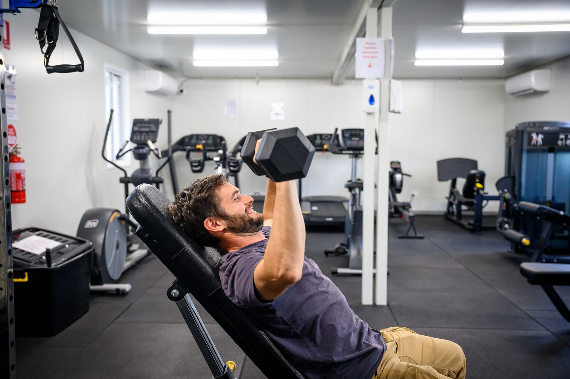 Man on an inclined bench lifting dumbbells in a gym, workout equipment visible.