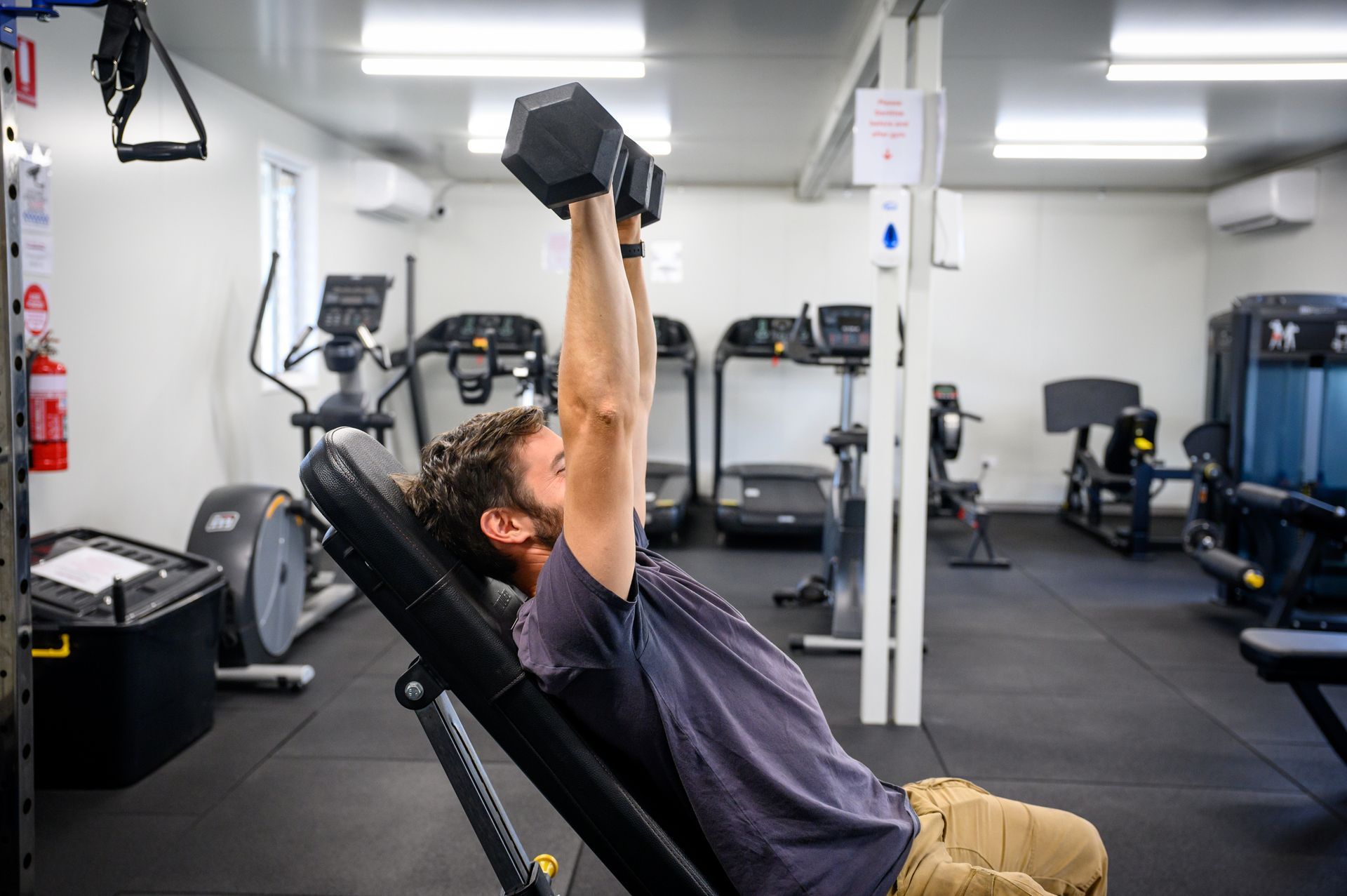 Man doing dumbbell chest press on an inclined weight bench in a gym.