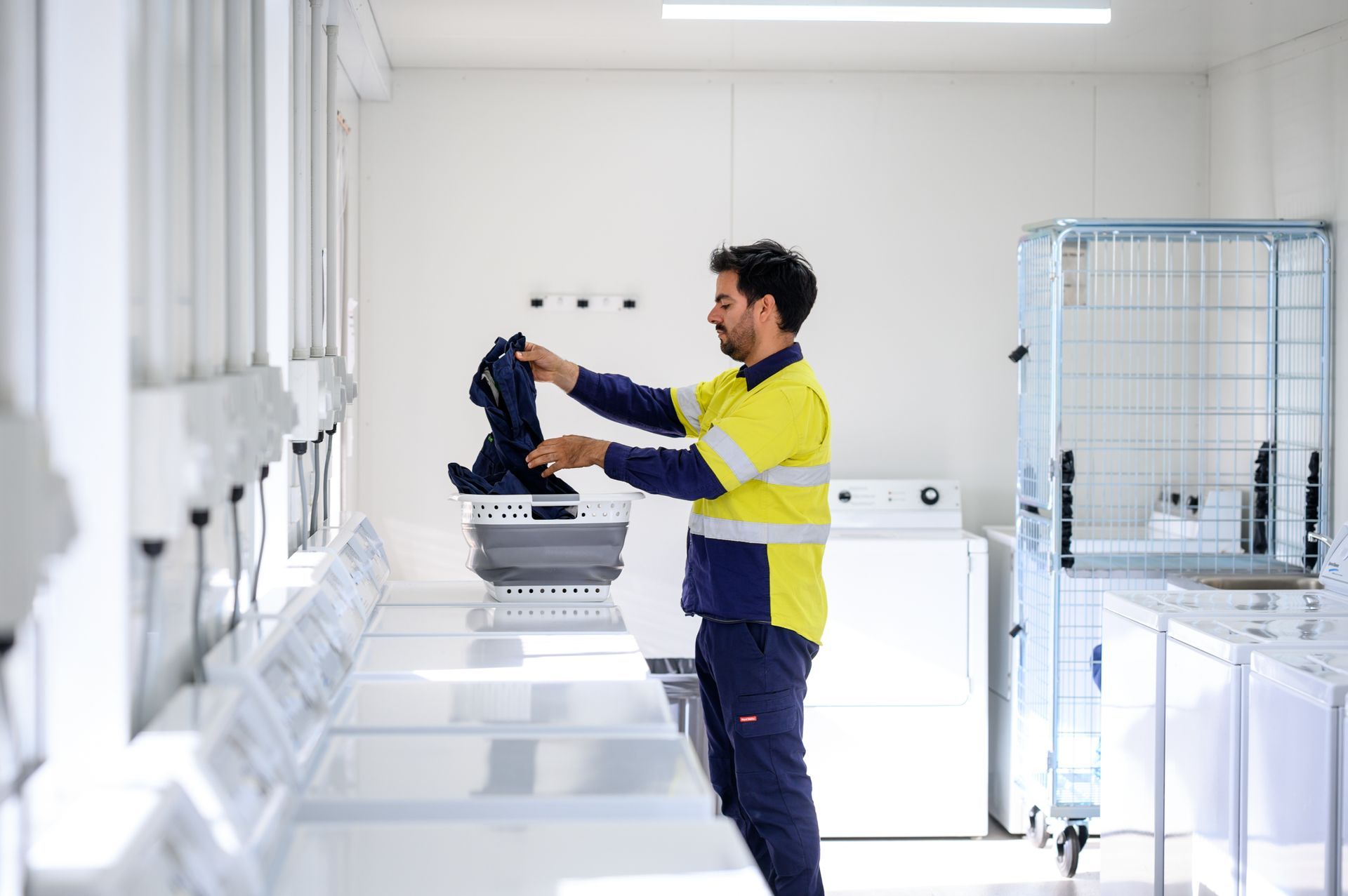 Person in work clothes loading clothes into a washing machine in a well-lit laundry room.