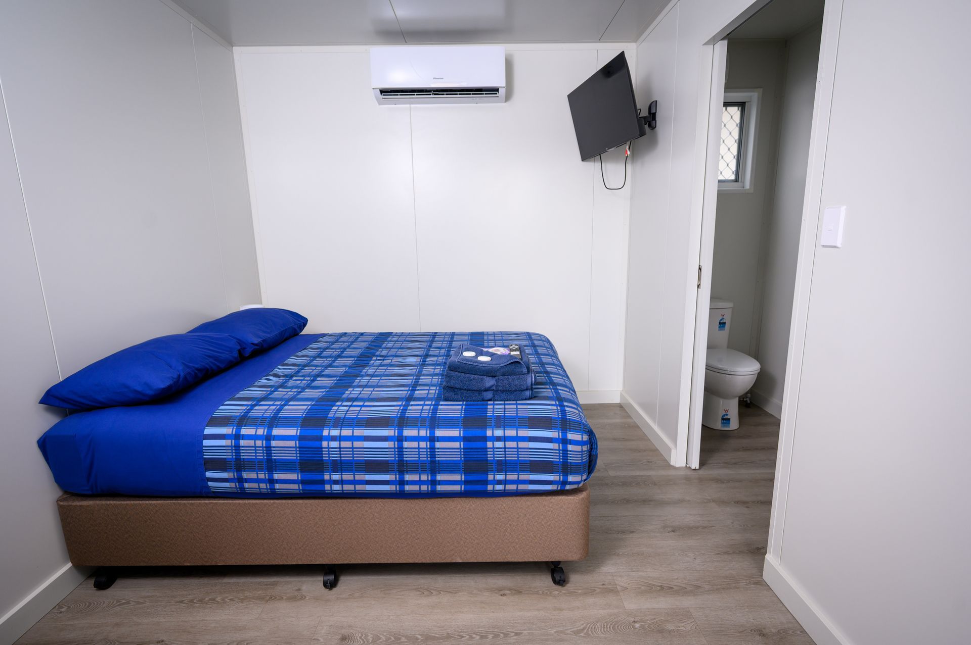 Small room with a bed, TV, air conditioner, and doorway to a toilet.
