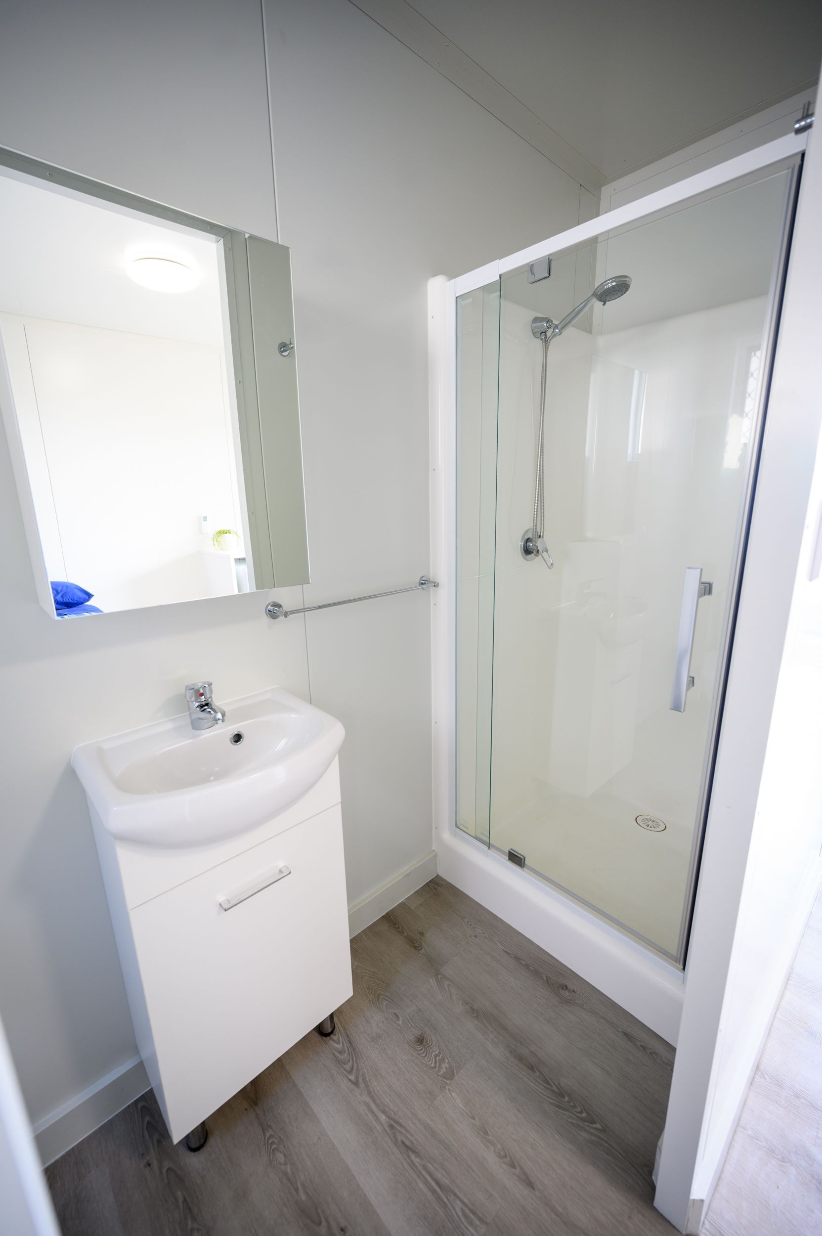 Bathroom with white walls, a shower, sink, mirror, and gray floor.