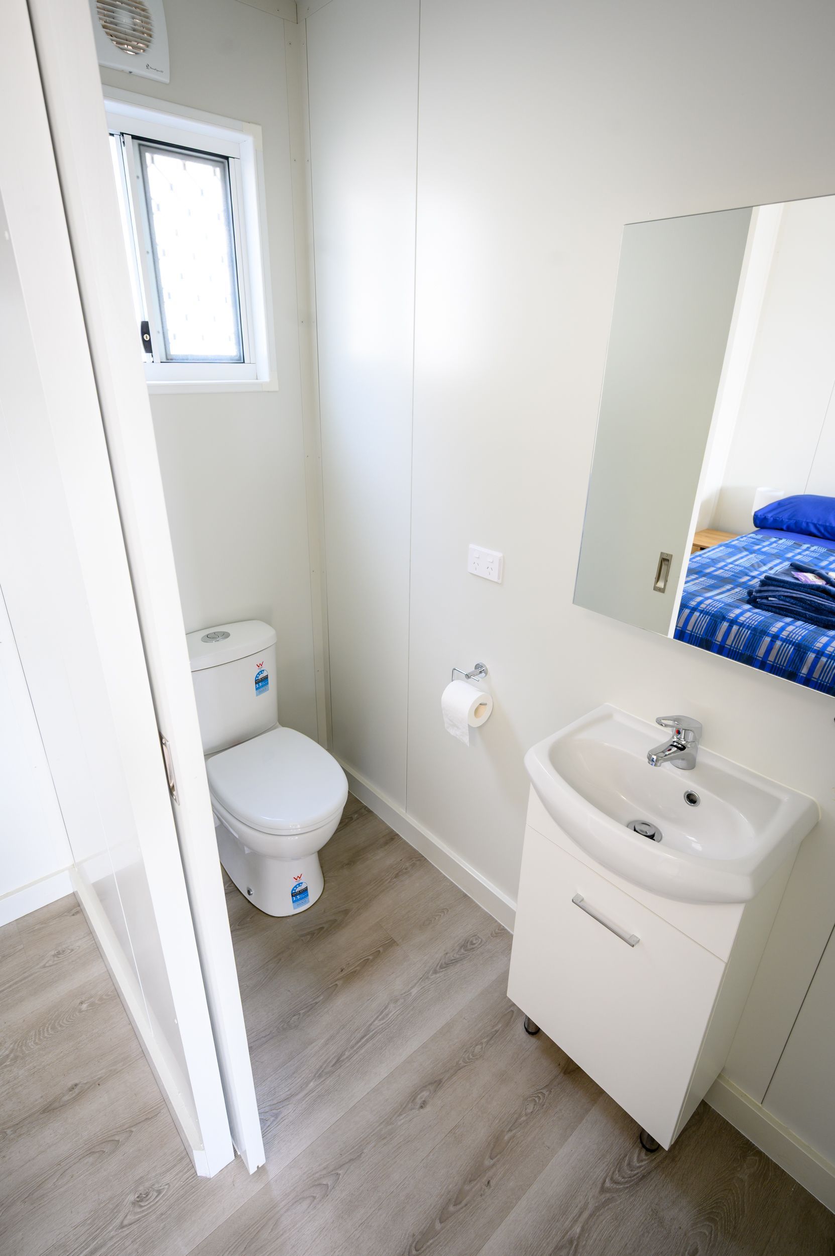Bathroom with toilet, sink, mirror, small window, and light wood-look flooring.