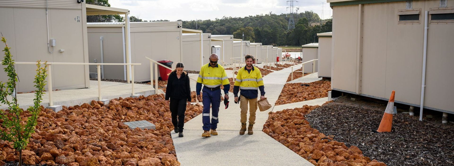Three workers walking along a landscaped path between modern accommodation units at Collie Hills Village.
