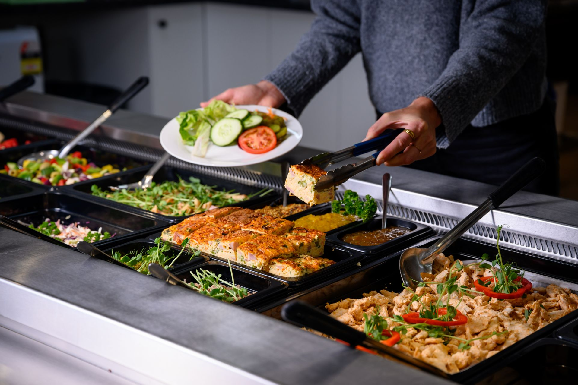 Person using tongs to serve food from a buffet. Salad plate in hand.