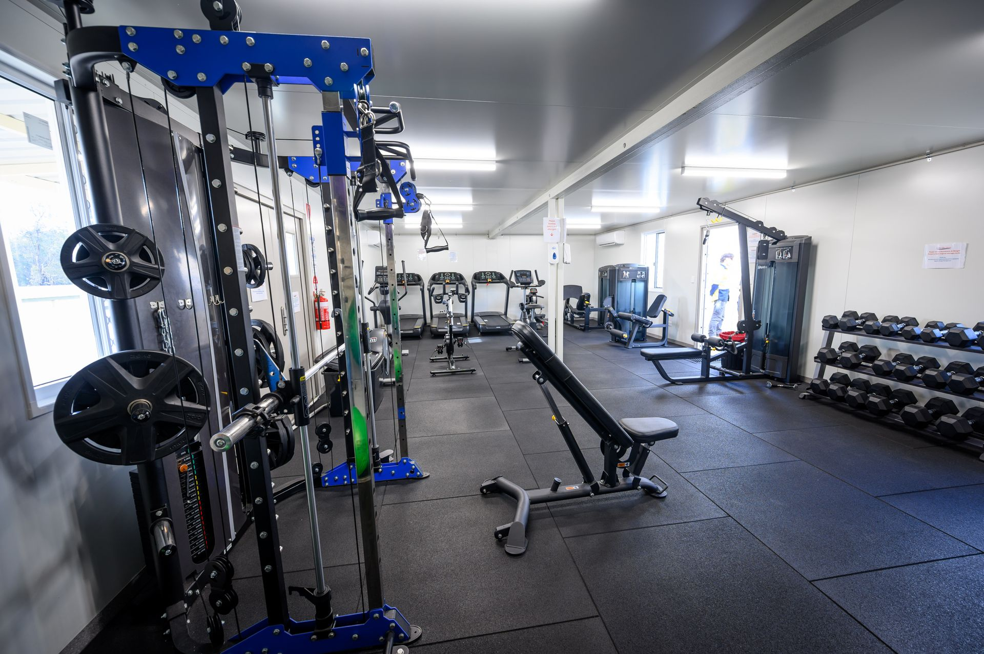 Gym interior with weight machines, benches, and free weights on a rubber floor.
