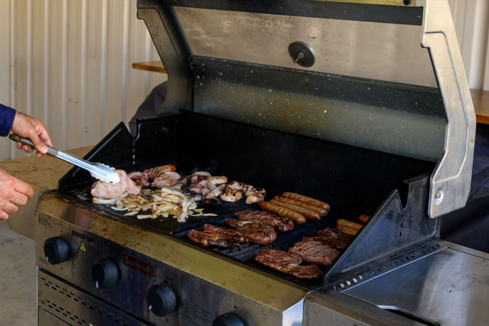 Person using tongs on a grill cooking meat and onions outdoors at Collie Hills Village.