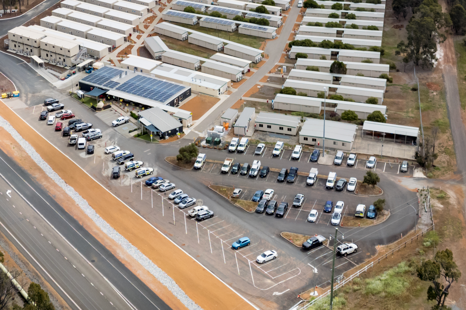 Aerial view of a complex with many modular buildings, a parking lot with cars, and a road.