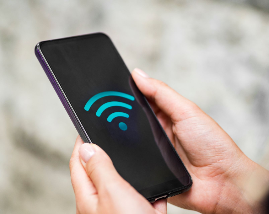 Person holding a smartphone displaying a blue Wi-Fi signal icon on the screen.