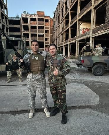 Two soldiers are posing for a picture in front of a building.