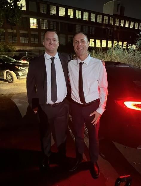 Two men in suits and ties are posing for a picture in front of a car.