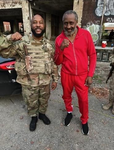 Two men in military uniforms and red sweatpants are posing for a picture.