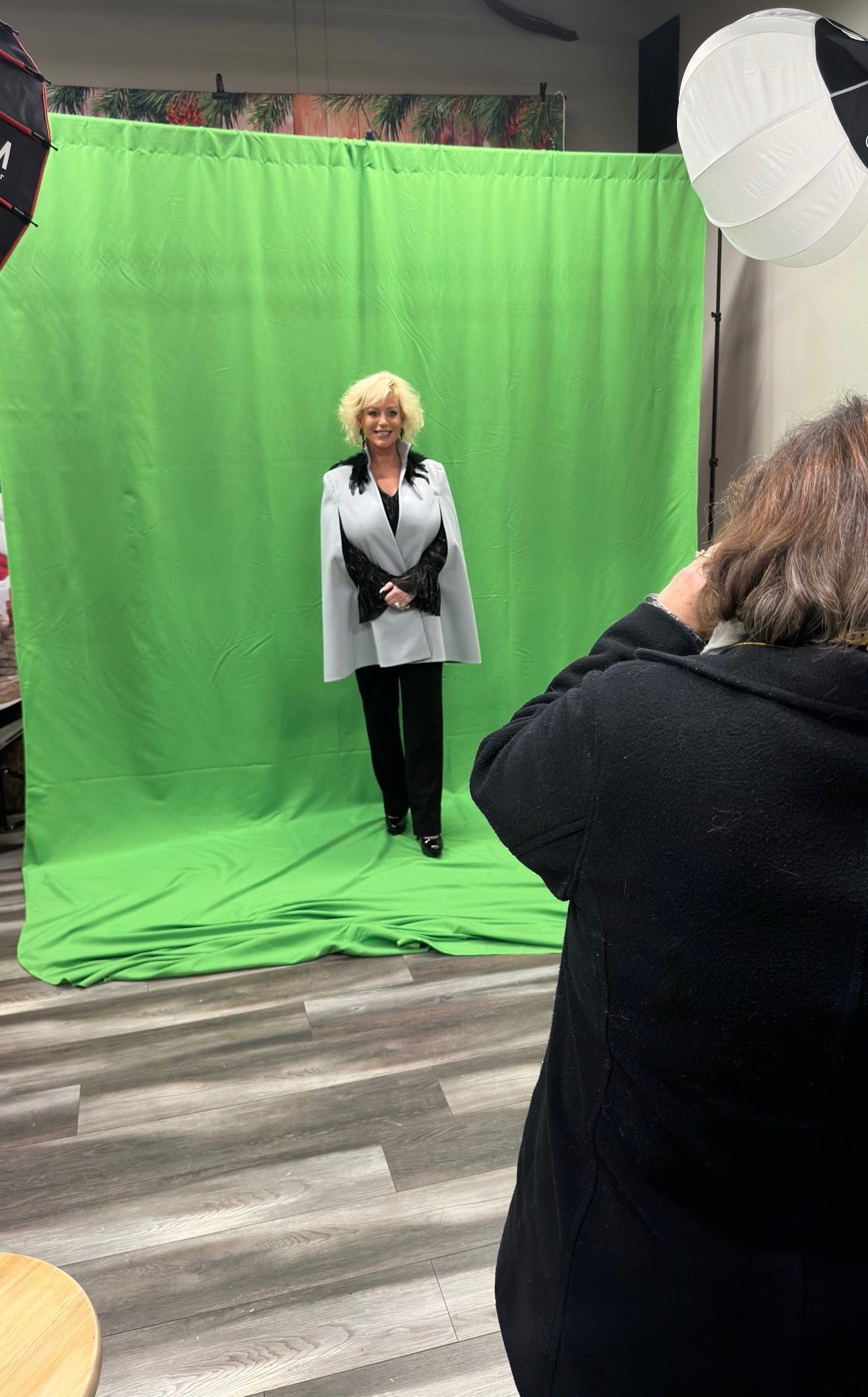 A woman is standing in front of a green screen holding a notebook.