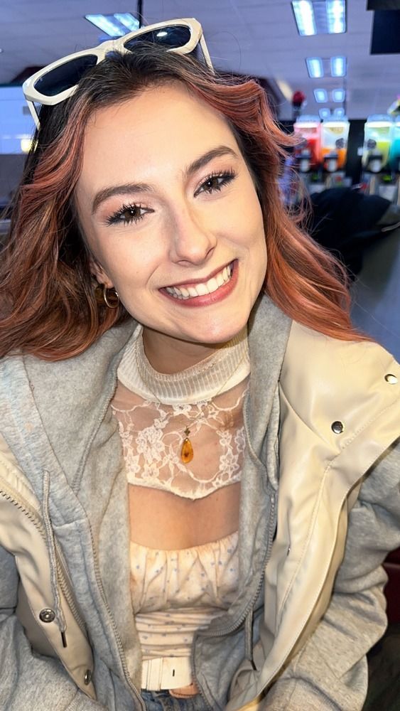 A woman wearing sunglasses and a jacket is smiling for the camera.