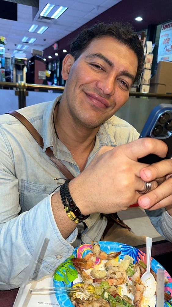 A man is sitting at a table with a plate of food and a cell phone.