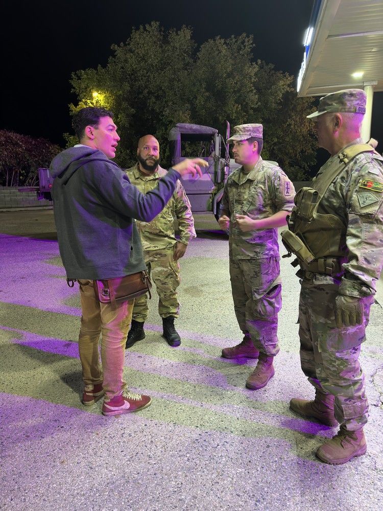 A group of soldiers are talking to a man in a parking lot.