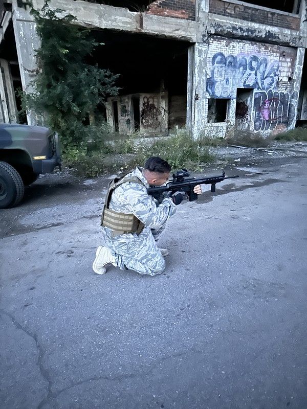 A man is filming a scene in the movie Tweed holding a rifle.