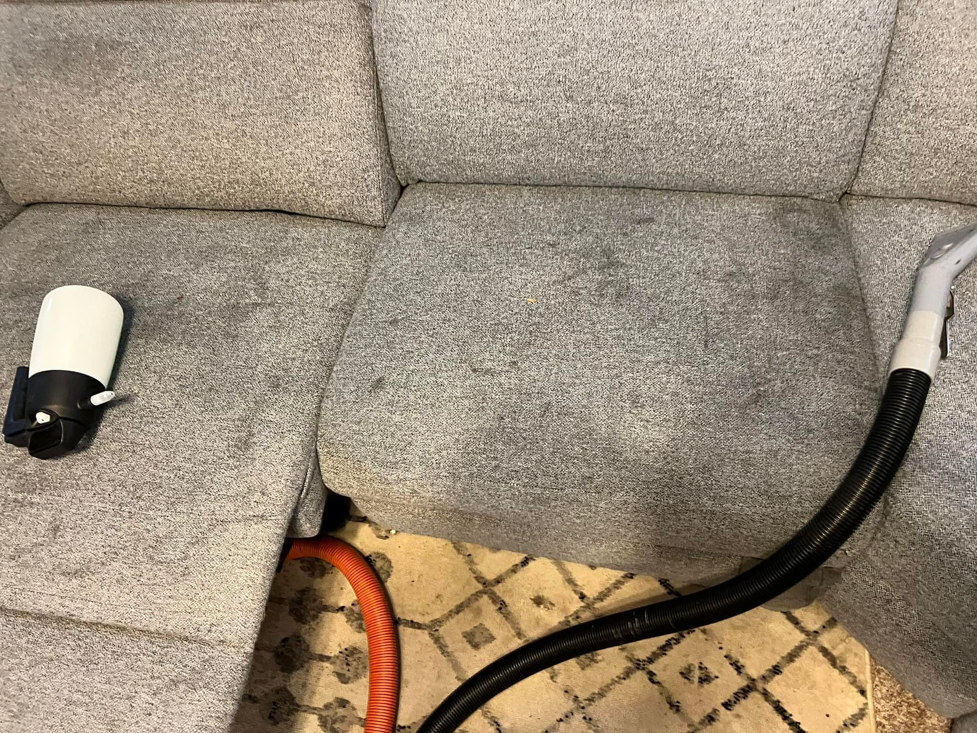 A man is cleaning a couch with a vacuum cleaner.