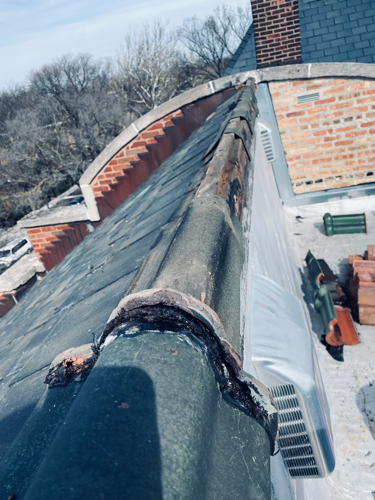 Damaged clay copings and shingled roof on historic building with radius parapet.