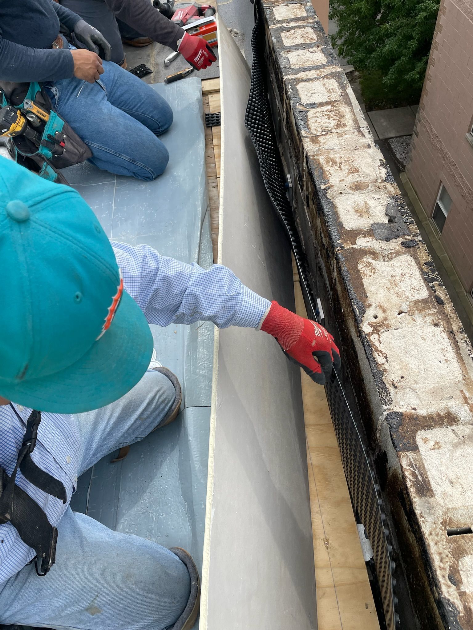 Workers placing dimple board against parapet wall