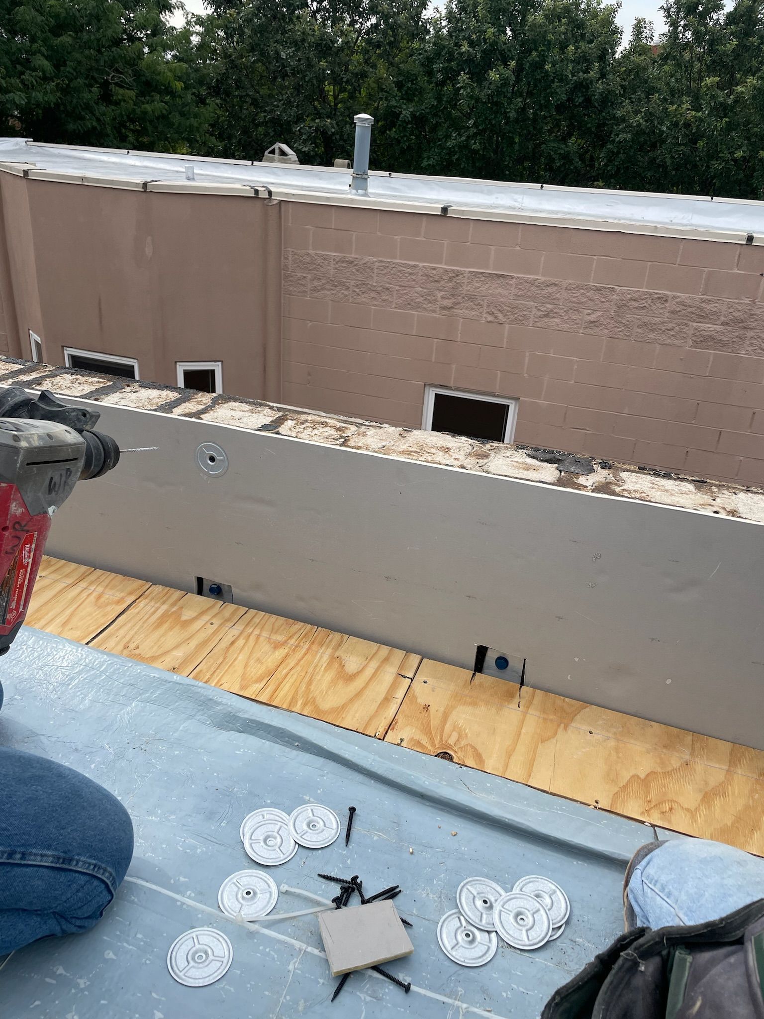 Worker drilling screws and washers to insulation wall against parapet wall