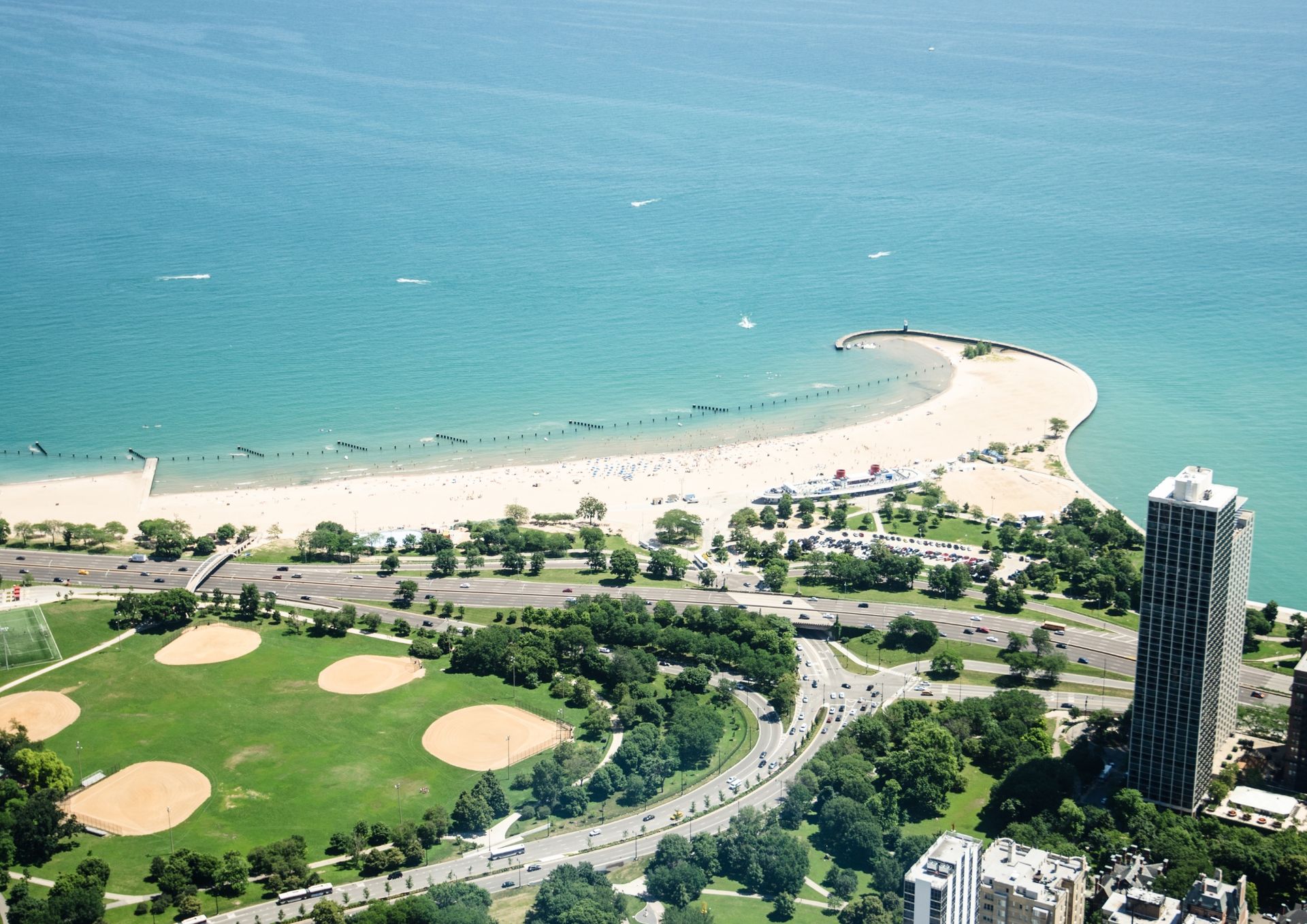 Aerial view of a curving sandy beach and turquoise water beside a golf course and tall waterfront buildings