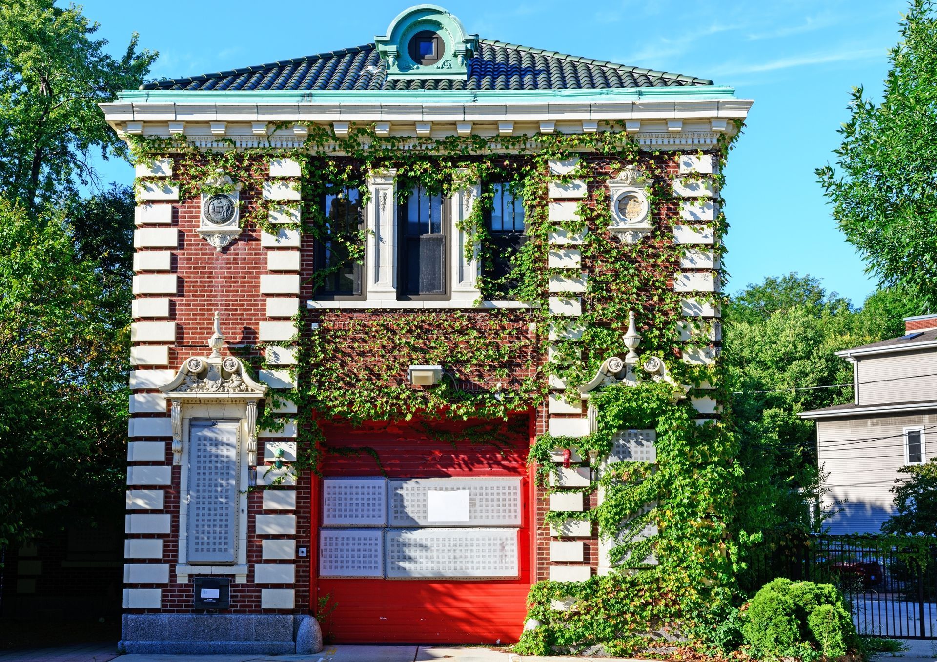 Small ivy-covered brick building(Firehouse) with red doors and white trim