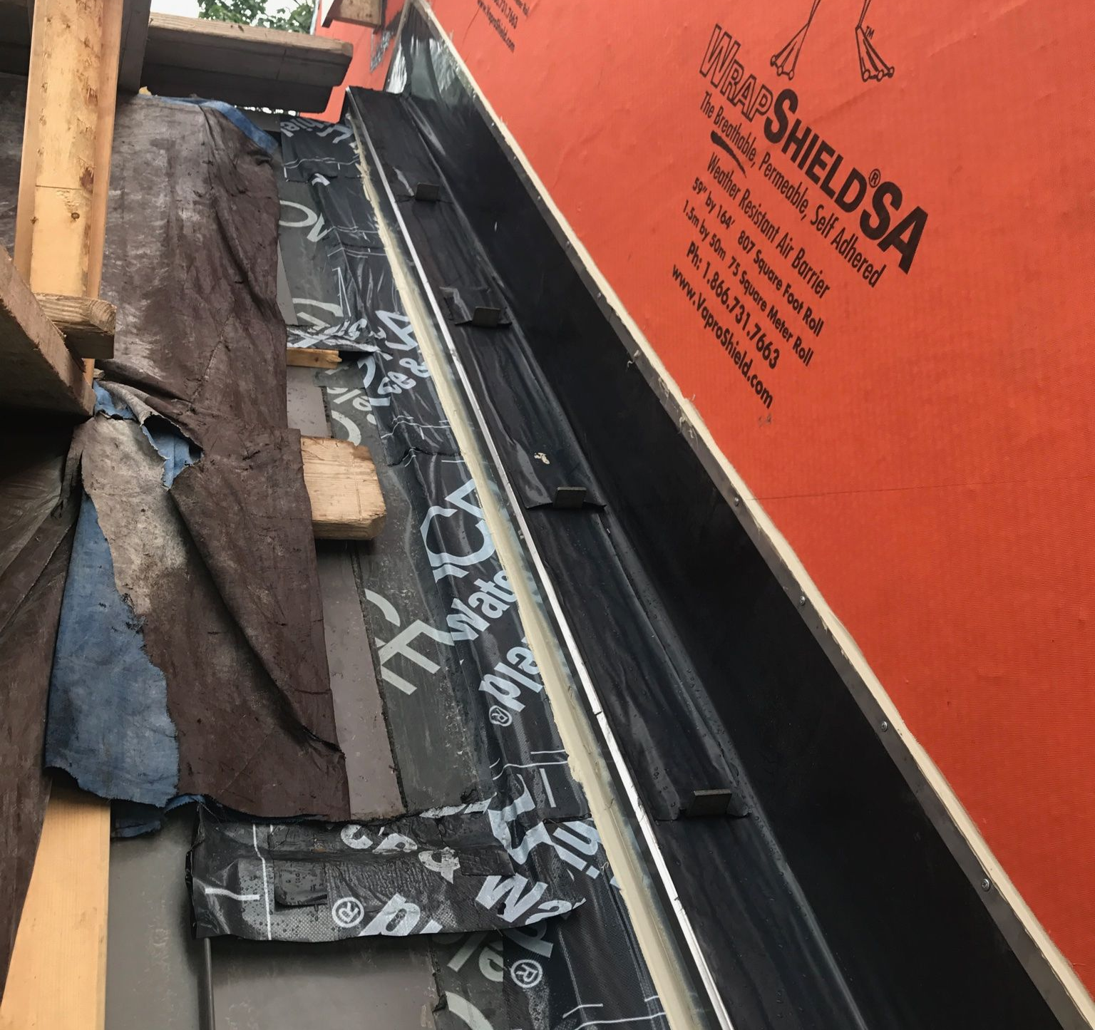 Damaged roof with torn underlayment beside a wall and wooden beams