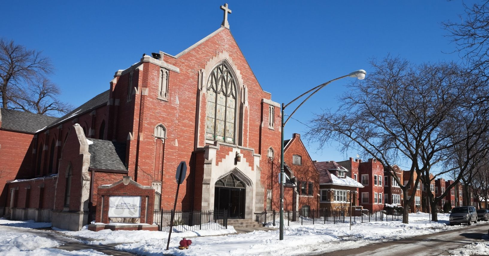 Snowy red-brick church with tall arched windows on a winter street corner