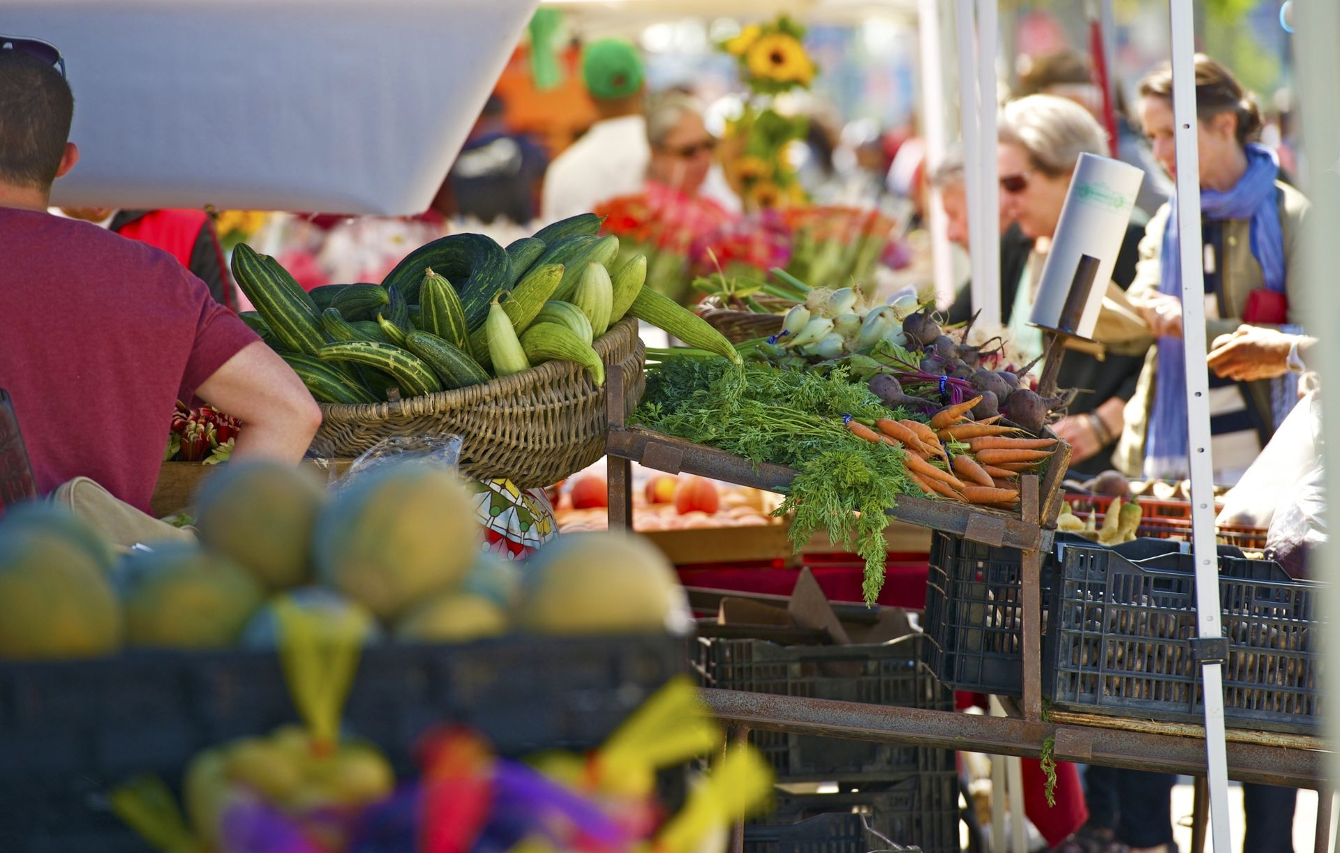 Outdoor farmers market with colorful produce on display and shoppers browsing stalls