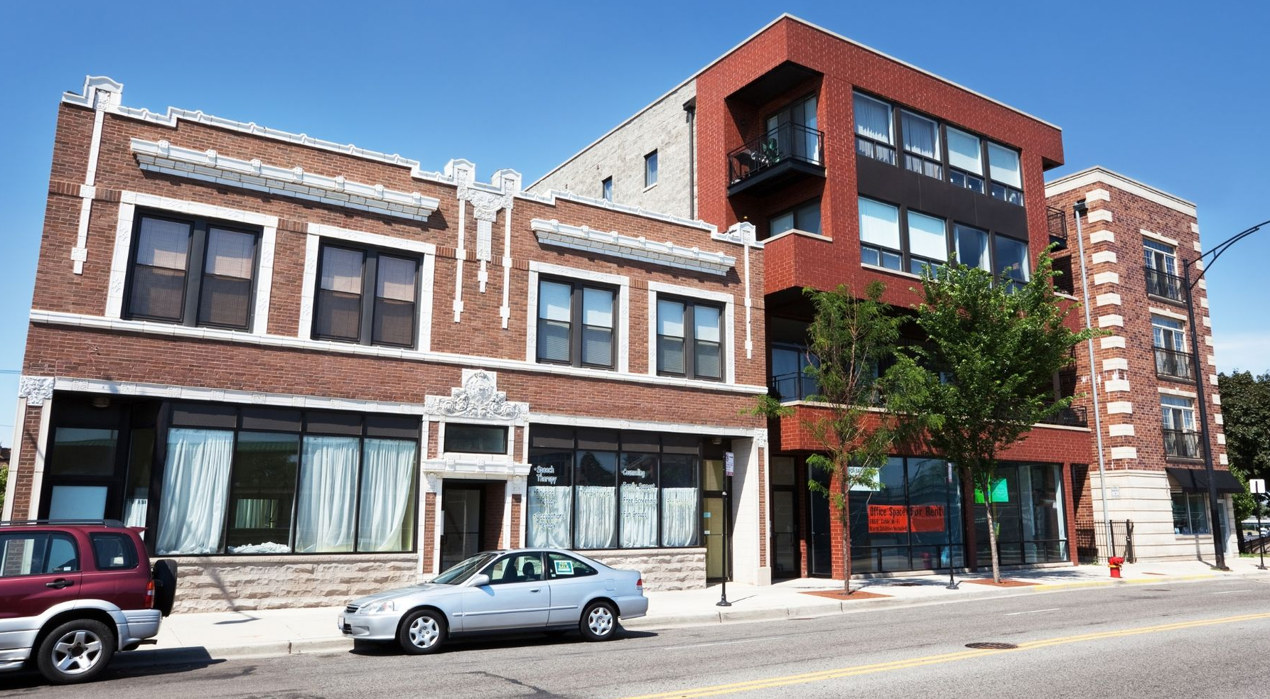 Brick storefronts and a modern red-brick building on a city street with parked cars