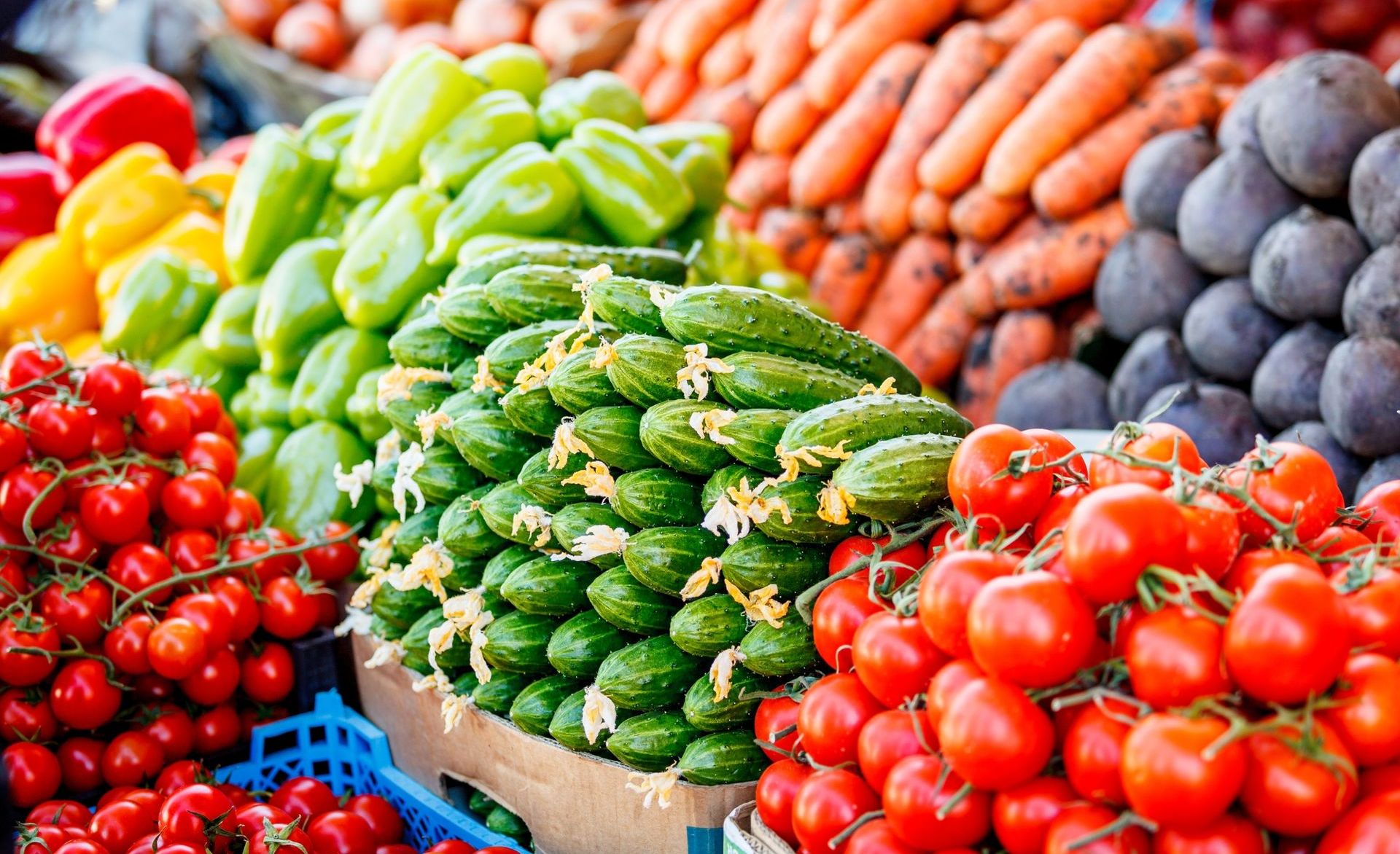 Colorful display of fresh vegetables at a market, including tomatoes, peppers, carrots, and artichokes