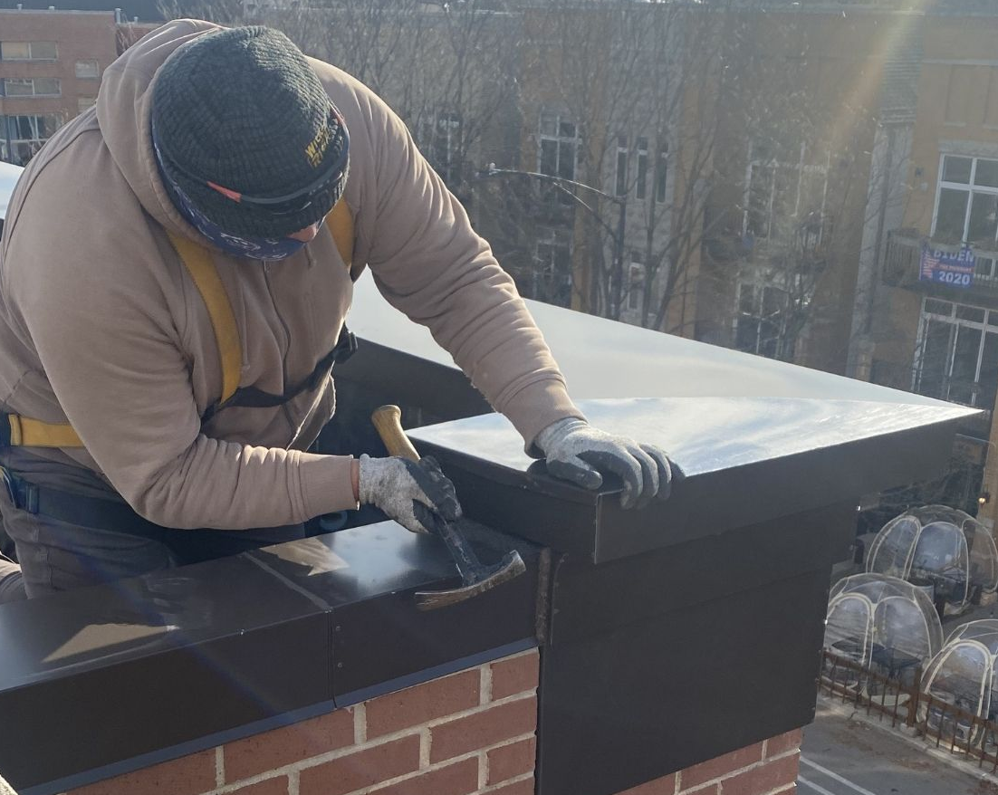 Worker installing a black flashing on top of a parapet wall