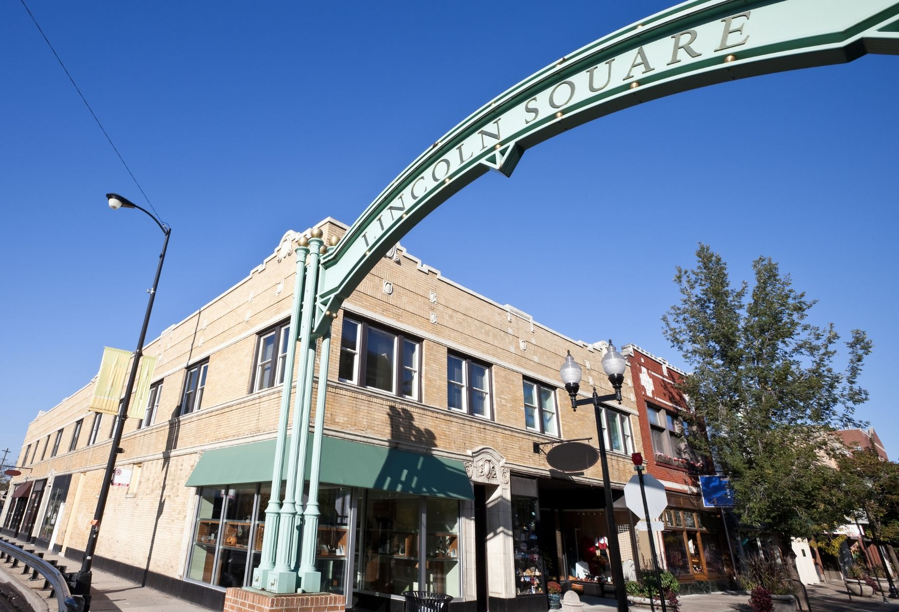 Downtown street scene with a green archway reading “Lincoln Square” over storefronts and buildings