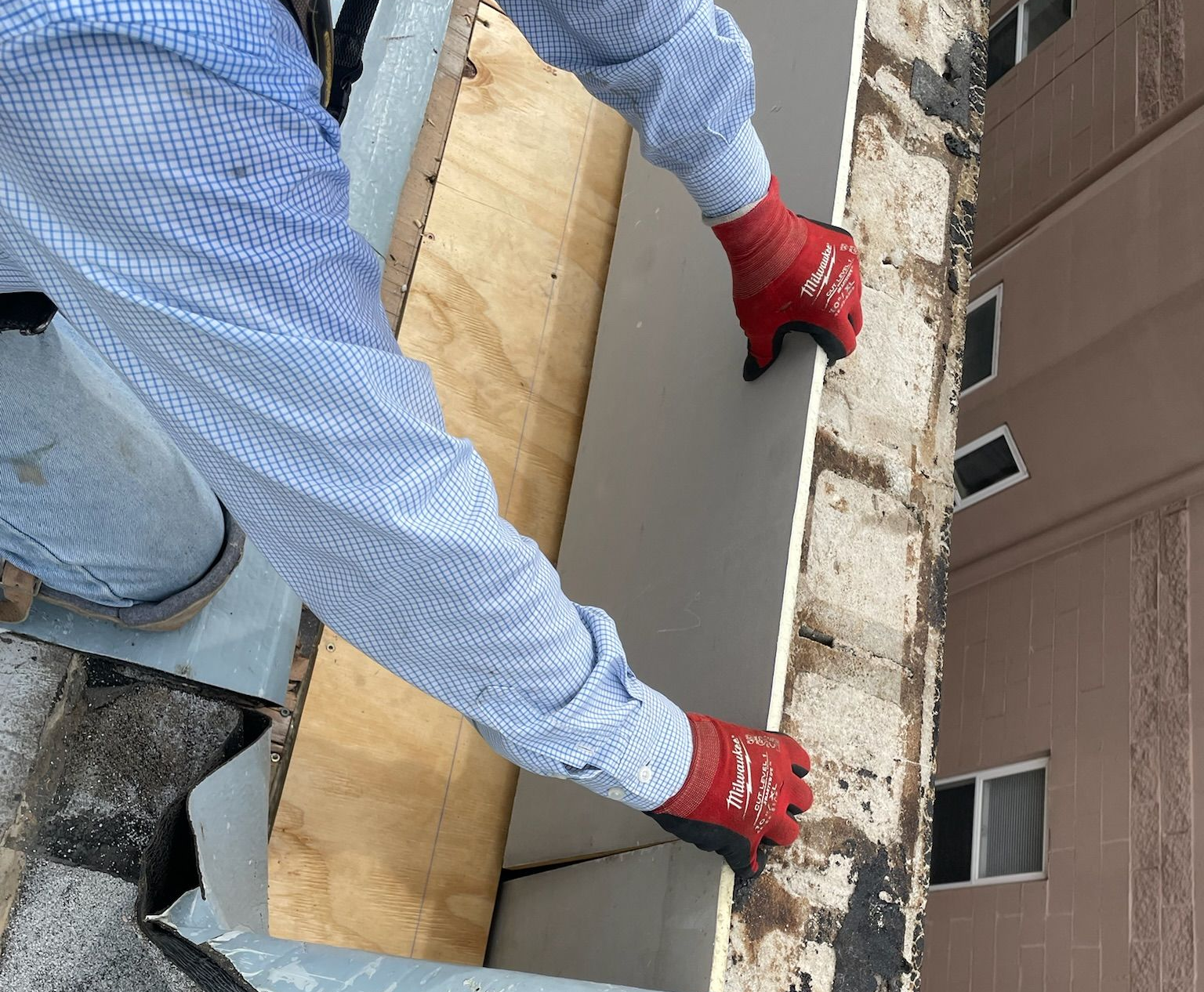 Worker positioning a large gray panel on a rooftop beside a wooden board and brick wall