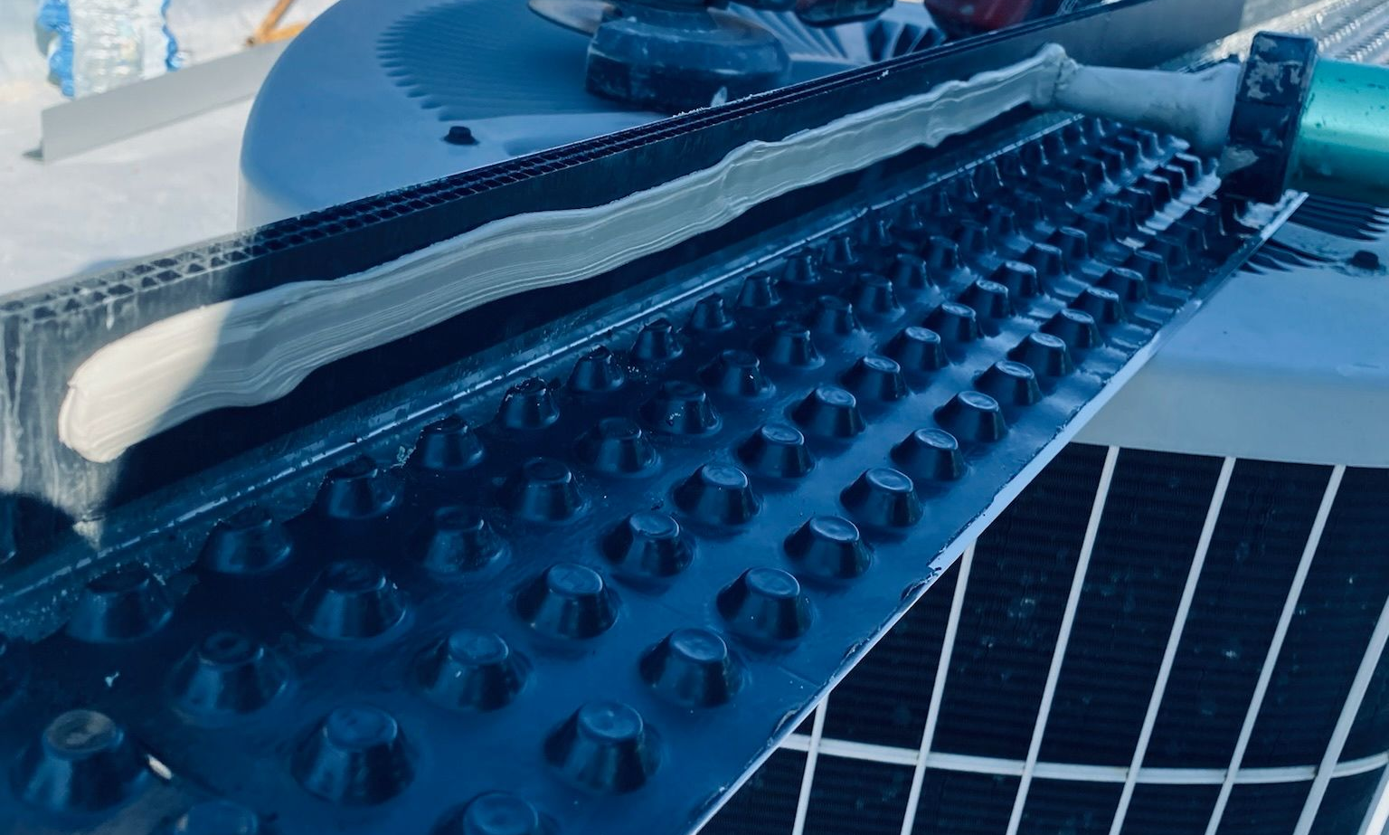 Close-up of a dimple board with caulk being applied on a plastic strip