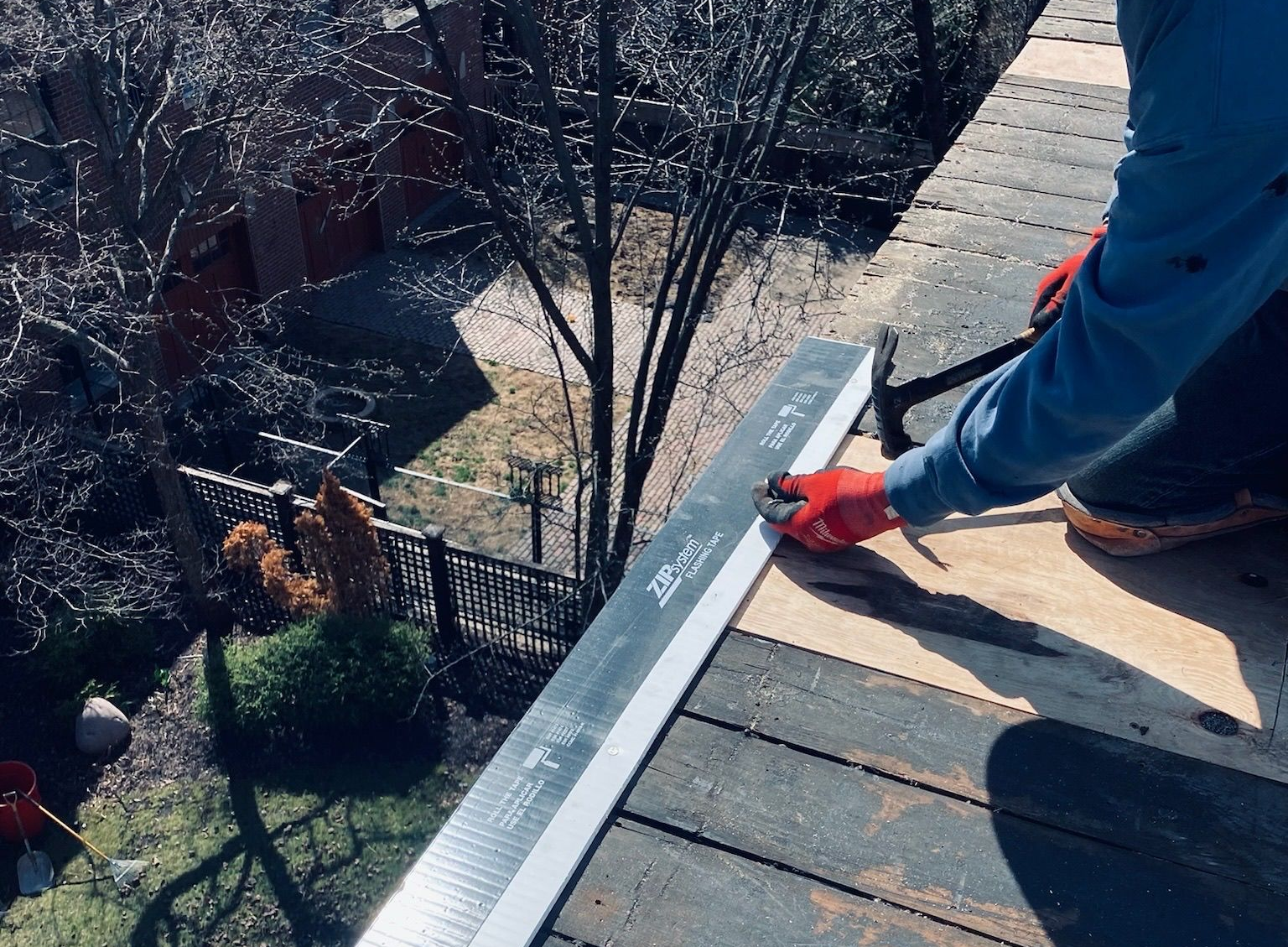 Worker using a utility knife to cut roofing material on a rooftop edge
